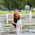 Attractive girl happily plays with fountain water stabs in city park