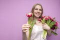 Attractive girl holds a bouquet of flowers on a pink background and gives one tulip, the seller offers flowers, a woman gives