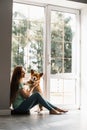 Attractive girl hug and play with corgi dog. Welsh Corgi Pembroke with his owner woman on the floor to ceiling window