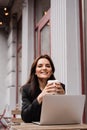 Attractive girl with laptop and cup of coffee is sitting outside of cafe. Young business woman with laptop is working Royalty Free Stock Photo