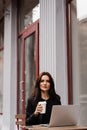 Attractive girl with laptop and cup of coffee is sitting outside of cafe. Young business woman with laptop is working Royalty Free Stock Photo