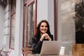 Attractive girl with laptop and cup of coffee is sitting outside of cafe. Young business woman with laptop is working Royalty Free Stock Photo