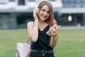 Pretty attractive girl is listening music from phone in headphones, typing messages, while walking on the urban street Royalty Free Stock Photo