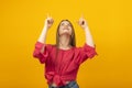 Attractive girl looks up and points her fingers at something. Young smiling woman pointing up, yellow background Royalty Free Stock Photo