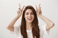 Attractive girl making air quotes. Portrait of charming young female raising hands near head and showing v or peace sign