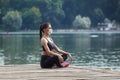 Attractive girl in a mask and sportswear is doing gymnastic exercises on a wooden pier in a city park. safe outdoor workout