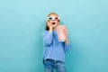 Attractive girl in movie glasses is holding popcorn in her hands on a light blue background wuth copyspace Royalty Free Stock Photo