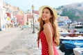 Attractive girl in Procida, Italy. Beautiful fashion woman with polka dots red dress and hat walks along the harbor of Procida