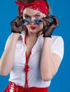 An attractive girl with a red bandana on her head attentively looks with lowered glasses. Girl in pin-up style isolated on blue ba