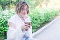 Attractive girl with red lips and manicure whith flower in her hair is sitting in the park and drinking coffee Royalty Free Stock Photo