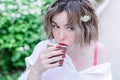 Attractive girl with red lips and manicure whith flower in her hair is sitting in the park and drinking coffee Royalty Free Stock Photo