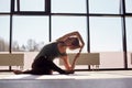 An attractive girl is sitting cross-legged, bending over, performing a yoga asana. The girl is doing yoga in a modern Studio with