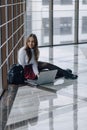 Attractive girl sitting on floor with laptop and things in airport terminal or office. travel atmosphere or alternative work