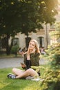 Attractive girl sitting on lawn in university park with books and smartphone in her hand, listening to music in headphones with Royalty Free Stock Photo