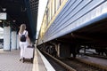 Attractive girl is standing with luggage at the station and waiting for the train, the student is going on a trip, she is walking Royalty Free Stock Photo