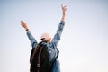 Attractive girl standing with raised hands against blue sky empty background. A happy traveler woman with a pink hat and