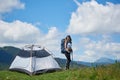 Woman tourist near camping in the mountains with backpack and trekking sticks in the morning Royalty Free Stock Photo