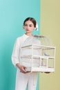 attractive girl in trendy white outfit with parrot in cage on turquoise