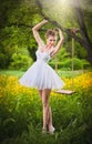 Attractive girl in white short dress posing near a tree swing with a flowery meadow in background. Blonde young woman