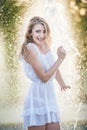 Attractive girl in white short dress sitting on parapet near the fountain in the summer hottest day Royalty Free Stock Photo