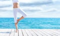 Attractive girl in white sporty clothes doing yoga on a wooden pier. Yoga, sport, leisure, recreation and freedom Royalty Free Stock Photo