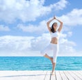 Attractive girl in white sporty clothes doing yoga on a wooden pier. Yoga, sport, leisure, recreation and freedom Royalty Free Stock Photo