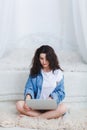 Attractive girl in white t-shirt and denim shirt, sits on the floor and uses a laptop . Royalty Free Stock Photo