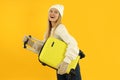 Attractive girl in winter clothes with luggage bag on yellow background