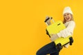 Attractive girl in winter clothes with luggage bag on yellow background
