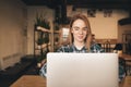 Attractive girl works on a laptop in a cozy cafe, looks at the screen and smiles. Beautiful blogger girl sitting with a laptop in Royalty Free Stock Photo