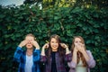 Attractive girls fool around and laugh on a summer day in the park. Three women cover their ears, eyes, and mouth on the natural