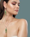Attractive glamorous woman with natural shiny clean skin wearing jewelry golden necklace with green pendant and long earring with