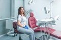 Attractive good-looking portrait of female dentist in clinic sitting on chair near dental unit with hands in blue gloves, smiling Royalty Free Stock Photo