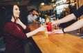 Attractive and gorgeous woman sitting at the stand and getting her order from barman. It is red cocktail. She looks to Royalty Free Stock Photo