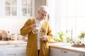 Attractive grandmother pouring water into glass in kitchen at home