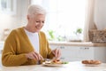 Attractive grandmother having lunch in kitchen alone