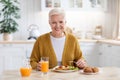 Attractive grandmother having lunch in kitchen alone