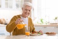Attractive grandmother pouring juice, having lunch in kitchen