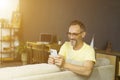 Attractive grey-haired man relaxing on a couch at home, using mobile phone. Handsome man in glasses texting in cellura phone Royalty Free Stock Photo
