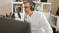 Attractive, grey-haired young hispanic man passionately lighting up the airwaves, speaking indoors at a professional radio studio, Royalty Free Stock Photo