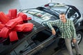 Attractive guy standing near big black auto with bow on top.