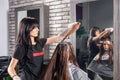 Attractive hairdresser holds in hand lock of brunette hair during process of dyeing hair of young woman