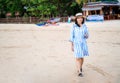 Attractive happy Asia woman walking alone on the island beach at Thailand. Wearing dress and hat, holding sun glasses and looking Royalty Free Stock Photo