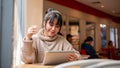 An attractive, happy Asian female is working remotely at a cafe co-working space, using her tablet Royalty Free Stock Photo