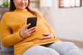 Attractive Asian pregnant woman using her smartphone on sofa in the living room. cropped shot Royalty Free Stock Photo