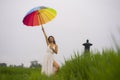 Attractive and happy Asian woman holding rainbow colorful umbrella or parasol  smiling playful outdoors at tropical green field in Royalty Free Stock Photo