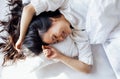 Attractive happy Asian woman lies on a white linen bed in the morning. The young girl smiles and enjoys waking up Royalty Free Stock Photo