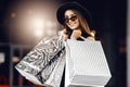 Attractive, happy, beautiful Shopaholic woman, in a black dress, black hat and sunglasses, stands with shopping bags in the city Royalty Free Stock Photo