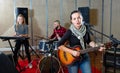 Attractive female soloist playing guitar and singing with her music band in sound studio Royalty Free Stock Photo