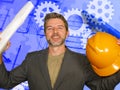 Attractive happy and confident industrial engineer man holding builder helmet and building construction blueprints on